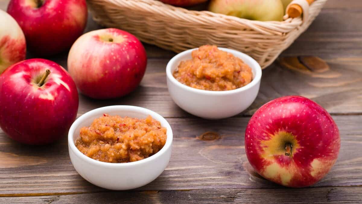 Fresh applesauce in bowls and red apples on a wooden table. ingredients for healthy holiday dog treats