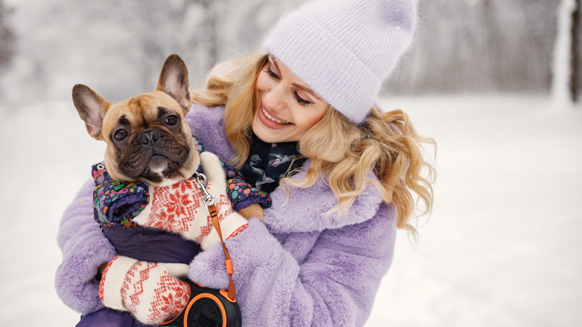 Woman in knitted hat playing with her dog french bulldog on a snow